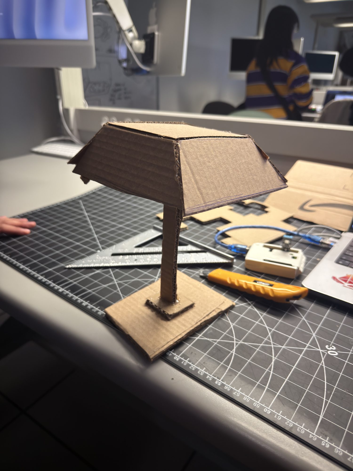 Step 3 — V2 stability upgrade: larger base and added support on the load side; shade attachment strengthened. Result: lateral sway is reduced and the model stays put during desk use. Next: improve cable routing and fine-angle adjustability.
