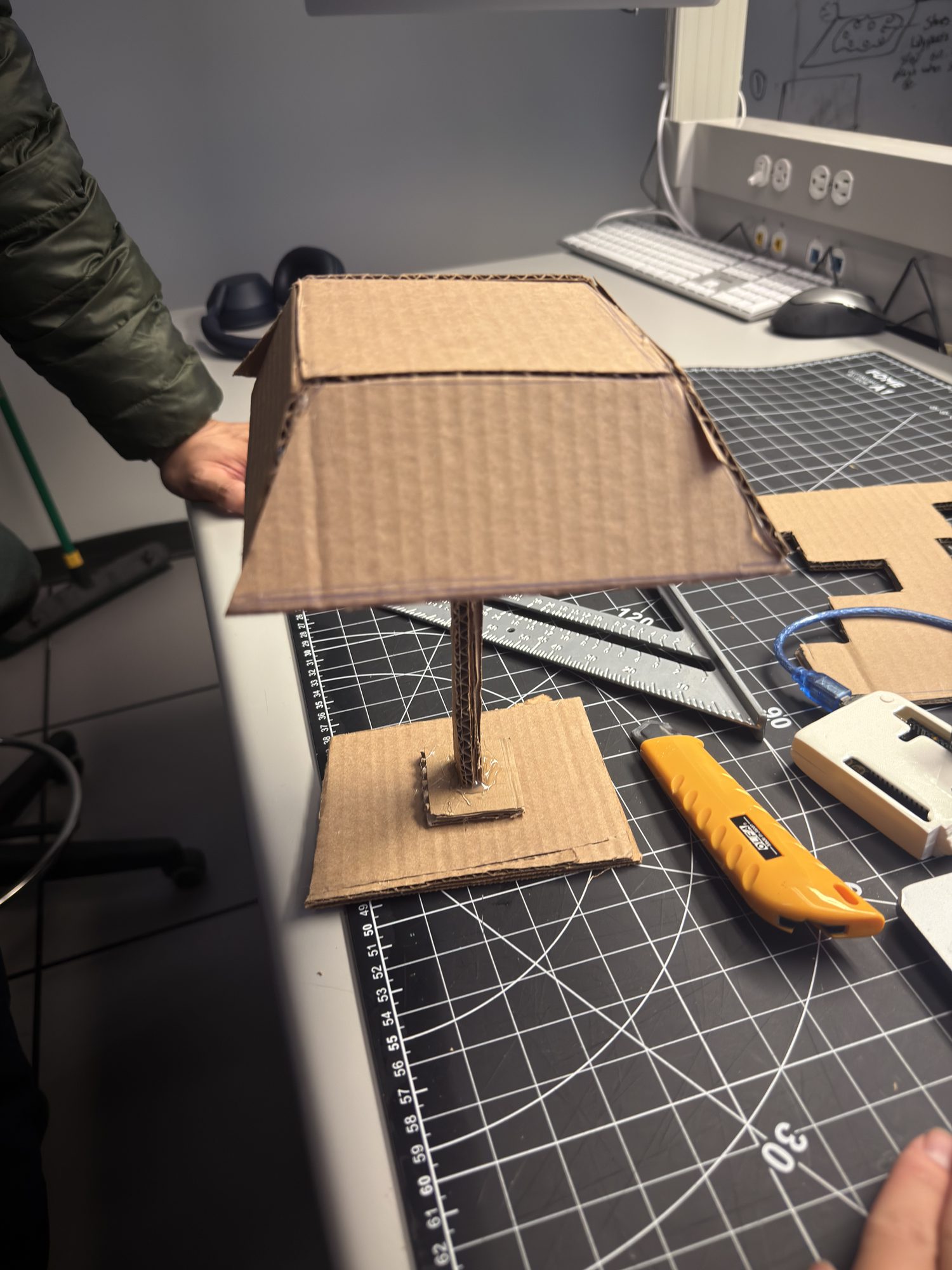 Step 4 — Joinery & cable planning: top view to inspect glue points and cardboard grain; leave channels and tie points for future light/sensor wiring. Hot-glue tacks + tape bridges keep it mod-friendly for revisions.
